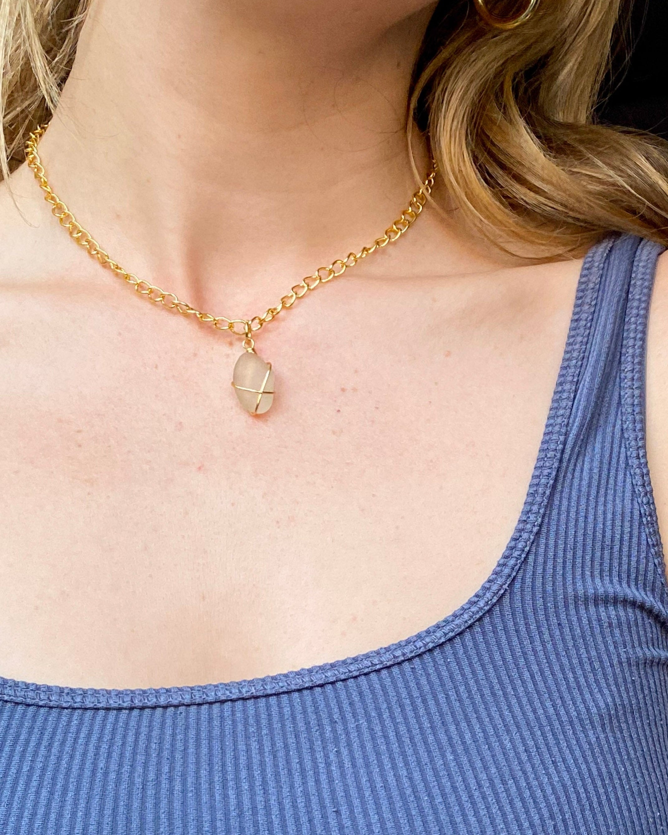 Person wearing a gold necklace with a clear pendant, visible under a blue sleeveless top.
