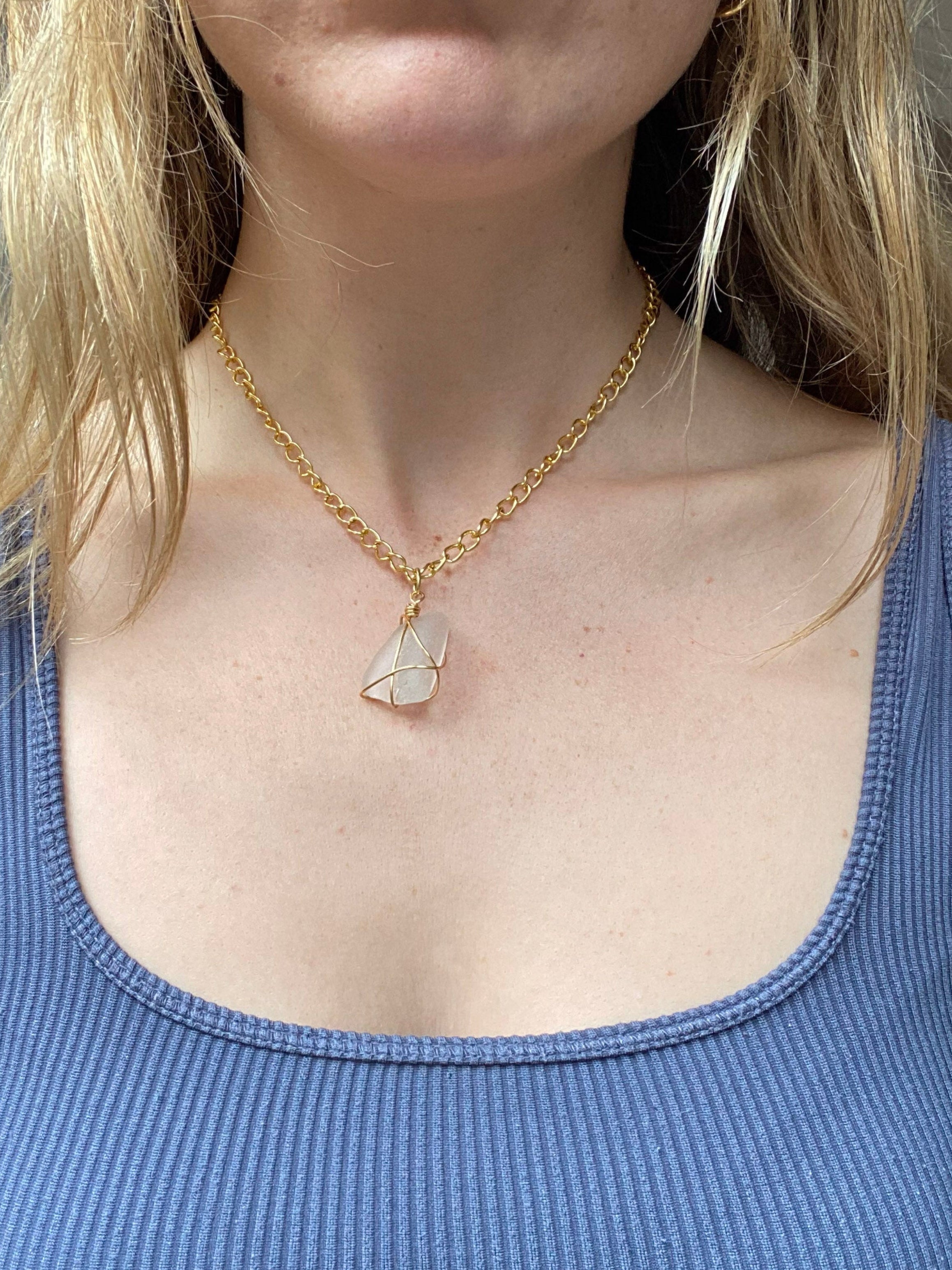 Person wearing a blue tank top and gold necklace with a pendant.