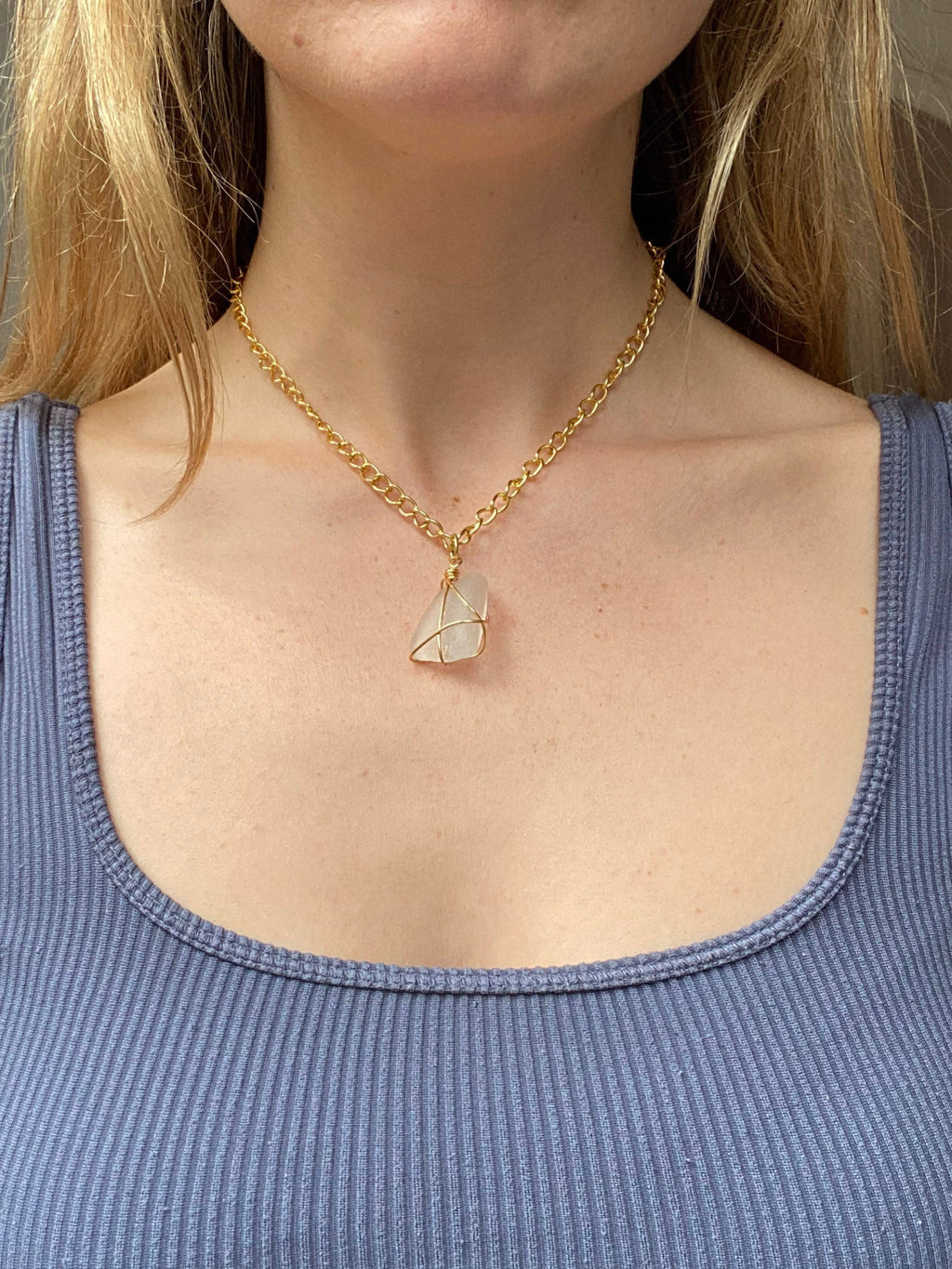 Person wearing a blue tank top and gold necklace with a pendant.