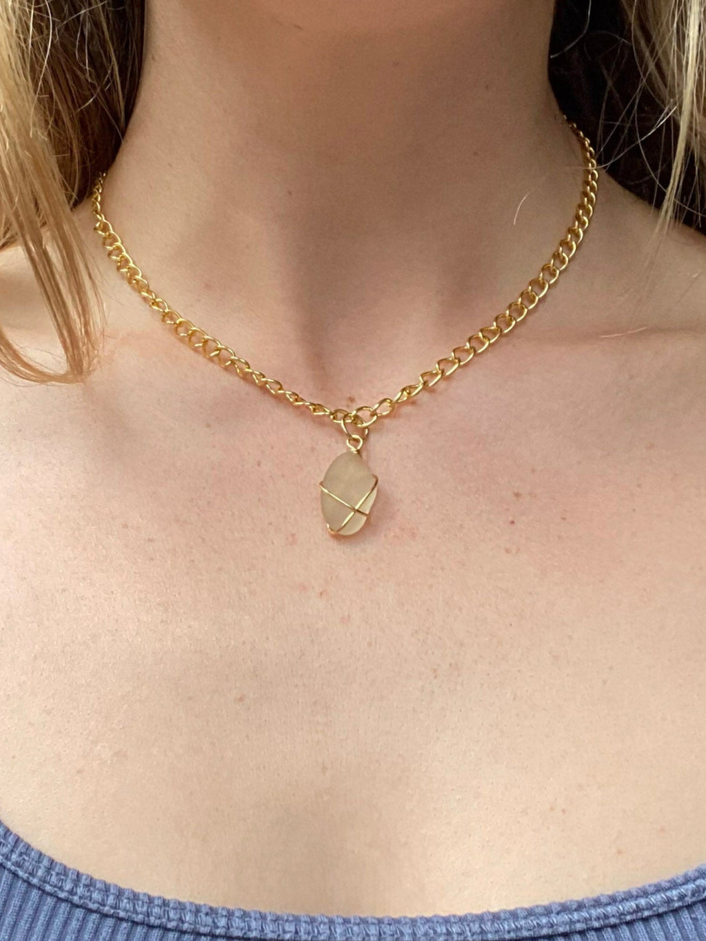 Person wearing a blue tank top and gold necklace with a pendant.