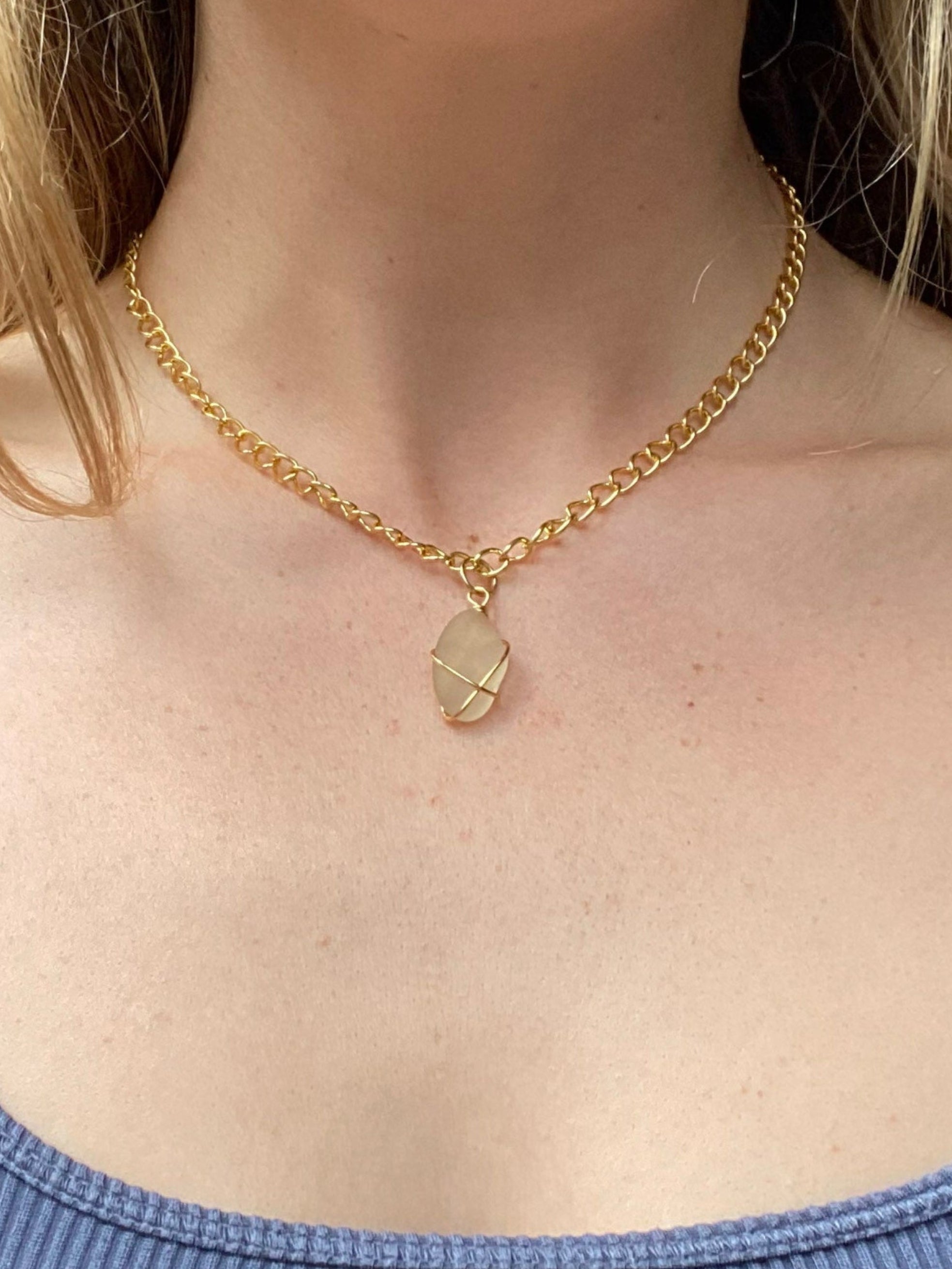 Person wearing a blue tank top and gold necklace with a pendant.