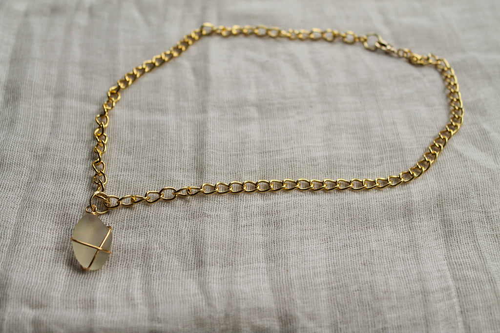 Gold chain bracelet with a small pendant on a textured gray surface