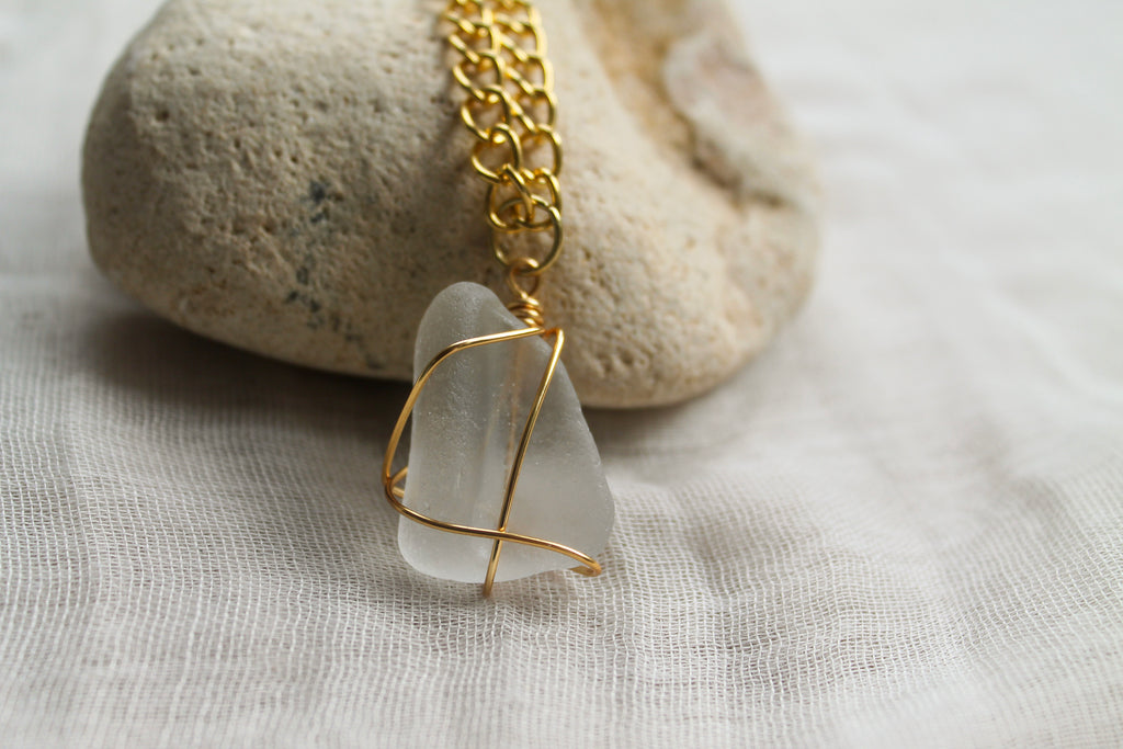 Necklace with a white pendant and gold chain on a stone and fabric background