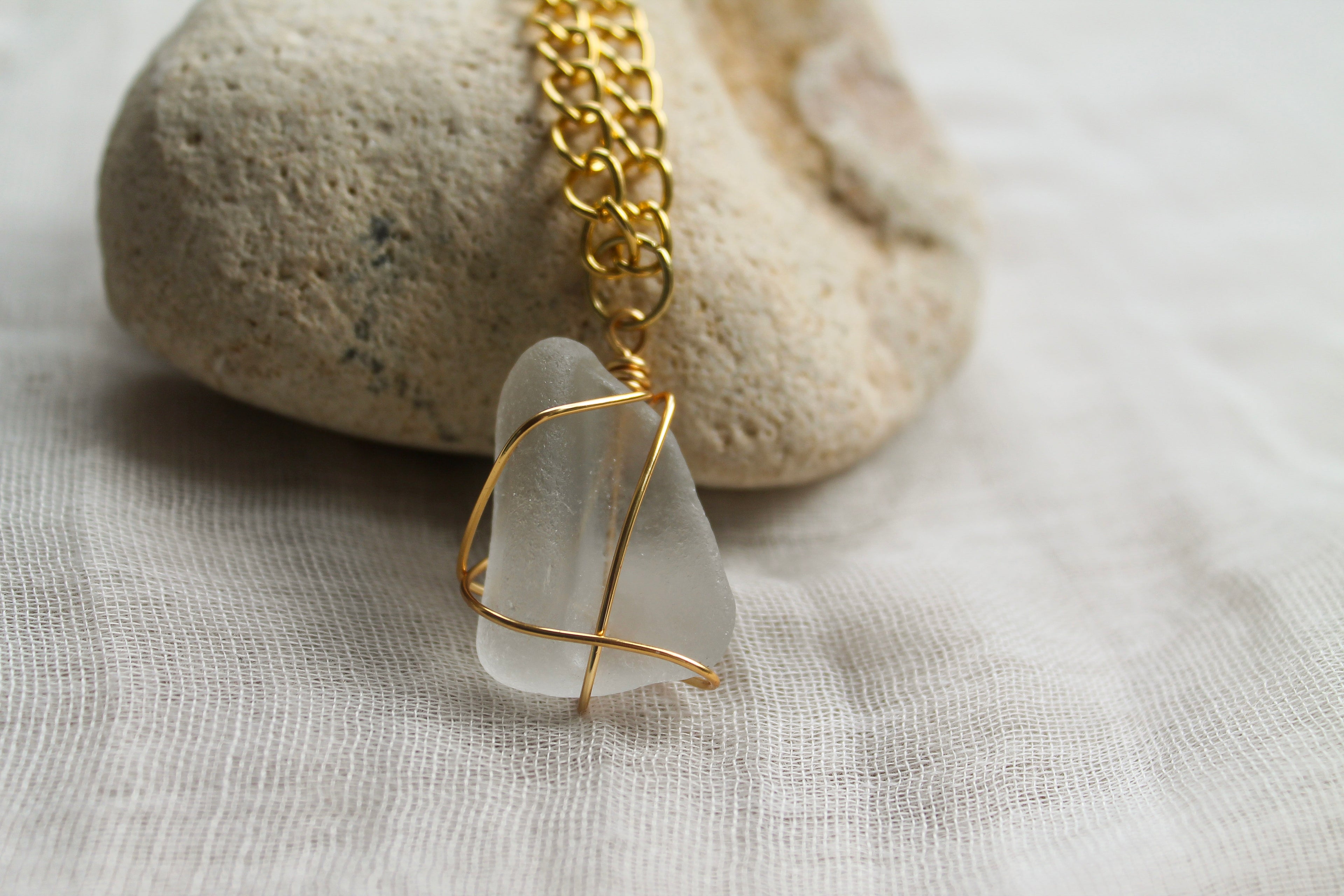 Necklace with a white pendant and gold chain on a stone and fabric background